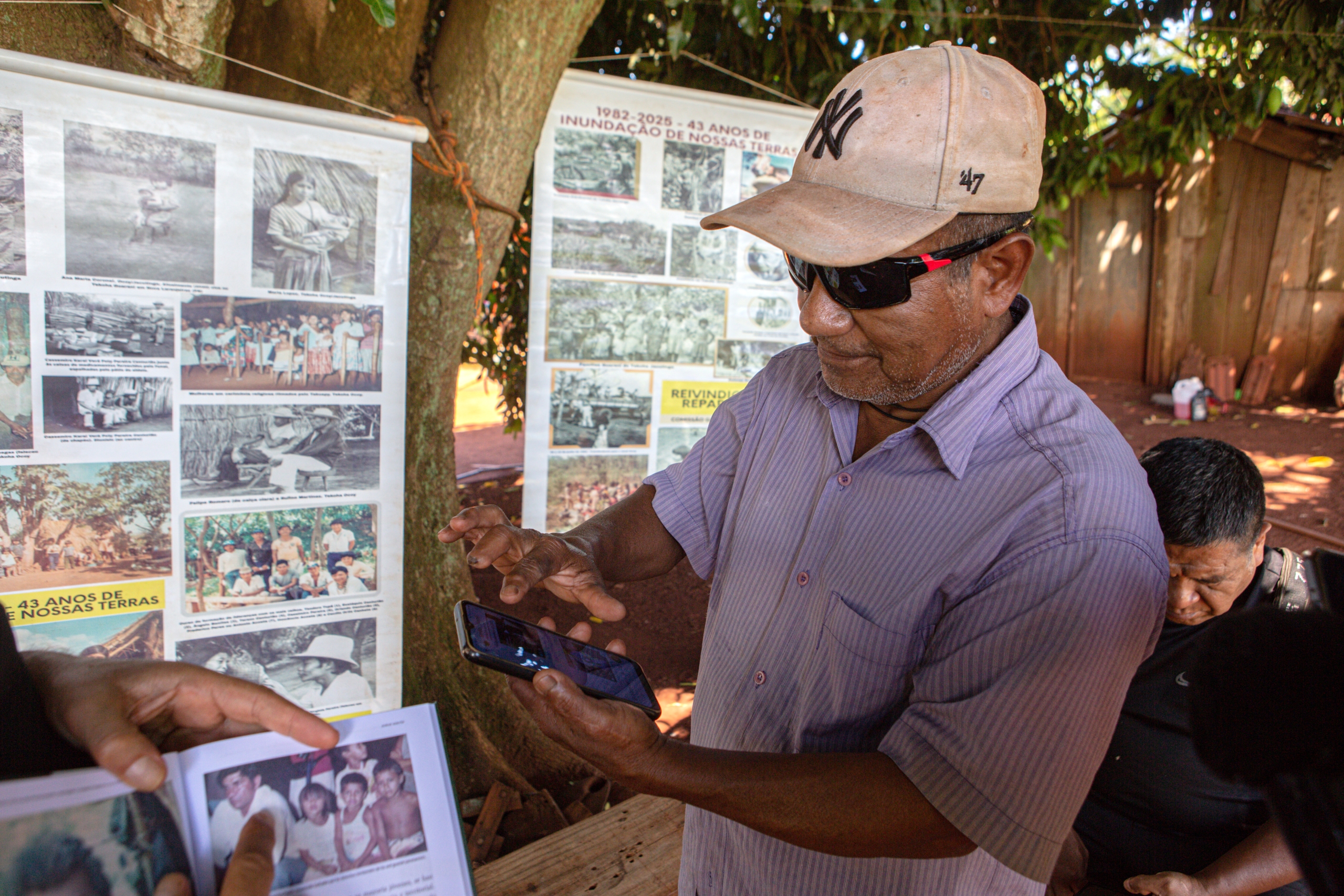 I Ocoy-samfundet nær Yguazu Nationalpark søger lederen Simón Paré Villavá efter fotos og dokumenter på sin mobiltelefon, for at diskutere deres igangværende kamp for retfærdighed mod Itaipu. Bag ham hænger et banner med arkivfotos, der er samlet over to år for at vise deres forbindelse til Paraná-floden.